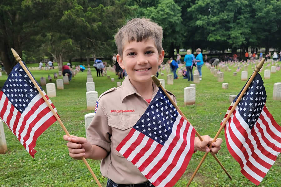 Boy holding miniature American flags on a cemetery, honoring local veterans